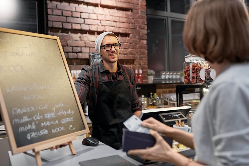 happy barman and woman paying money at cafe